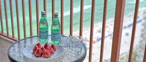 A table with two bottles of Pellegrino water, two glasses of water, and a plate with strawberries on a balcony overlooking the beach.