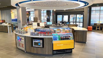 Una estación de autoservicio para bebidas y aperitivos, con una terminal de pago digital y un área de descanso con vistas al exterior.