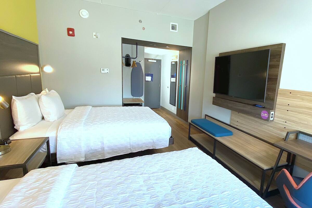 Ein Hotelzimmer mit zwei Betten, einem Fernseher, einem Schreibtisch und einer Bank.