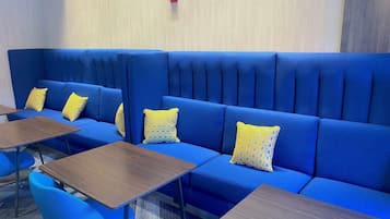 Un sofá azul con cojines estampados amarillos, una mesa de madera y una silla azul.