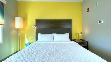 A hotel room with a bed, a bedside lamp, a nightstand, and a wall-mounted thermostat.