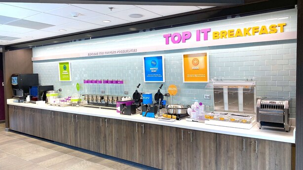 A breakfast counter with a sign reading "TOP IT BREAKFAST" and various food items and equipment. - Tru By Hilton Baltimore Harbor East, MD (Baltimore)
