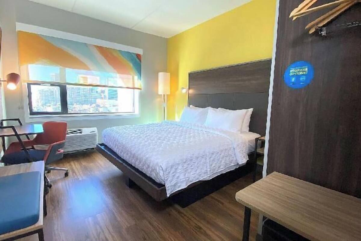 Ein Hotelzimmer mit Bett, Schreibtisch, Stuhl, einem Fenster mit Blick und einem Gepäckschild.