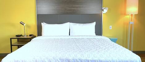 Een hotelkamer met een groot bed, een nachtkastje met een lamp, en een bijzettafeltje met een telefoon en oplader.