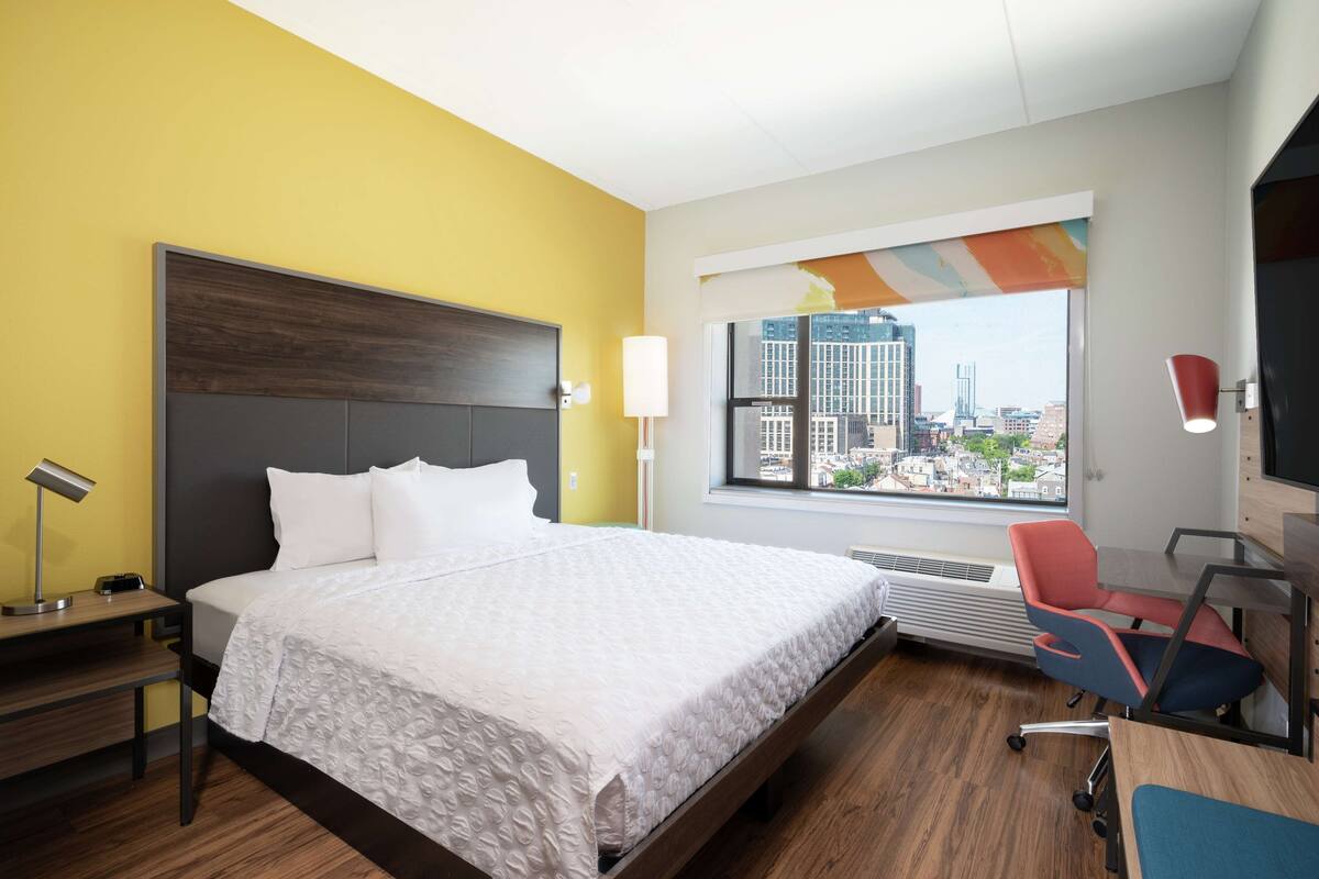 Ein Hotelzimmer mit einem großen Bett, einem Schreibtisch, einem Stuhl, einem Fenster mit Blick auf die Stadt und einer Heizung.