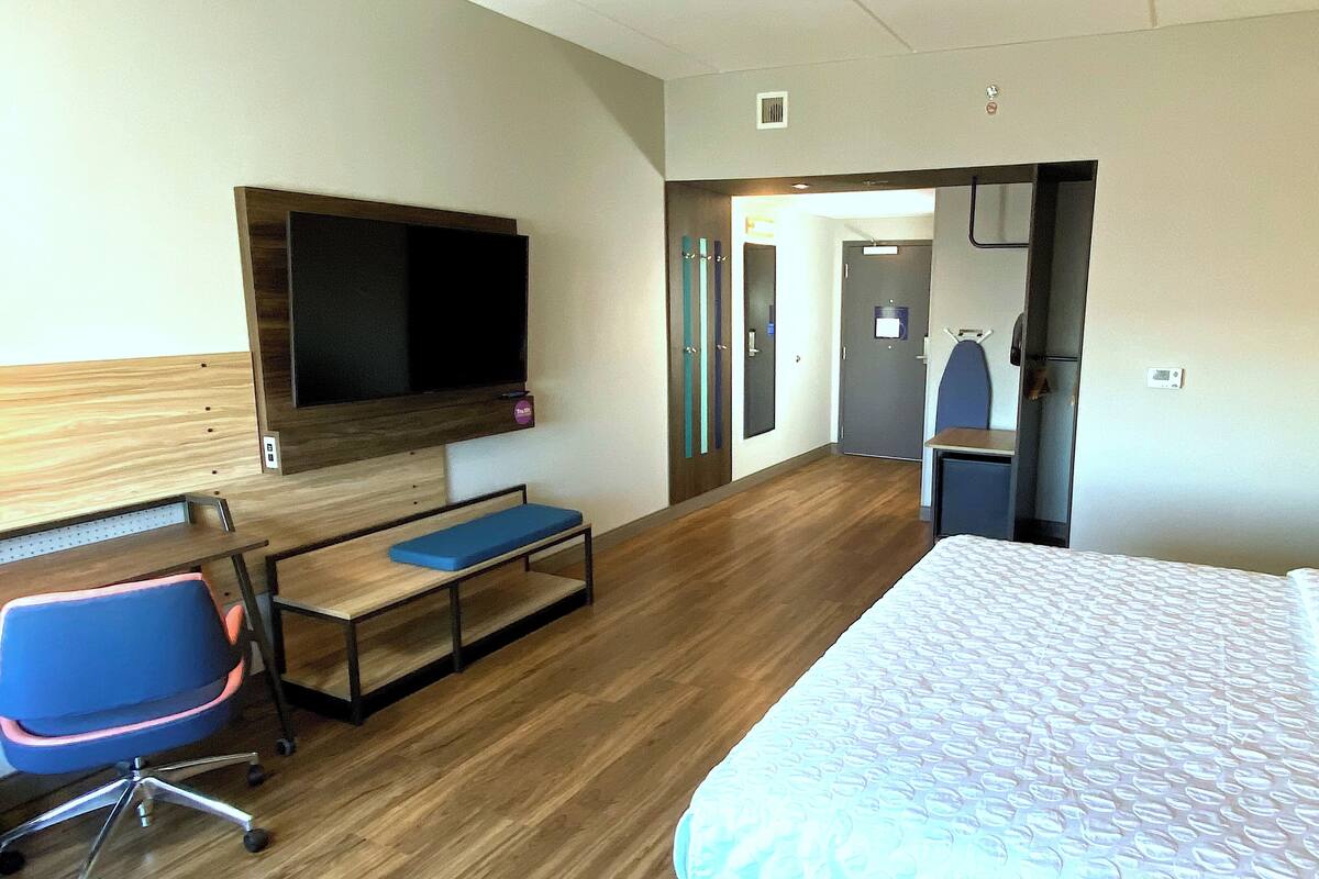 Ein Hotelzimmer mit einem Bett, einem Schreibtisch mit Stuhl, einem Fernseher und einer Tür zu einem Badezimmer.