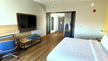 A hotel room with a bed, a desk with a chair, a television, and a door leading to a bathroom.
