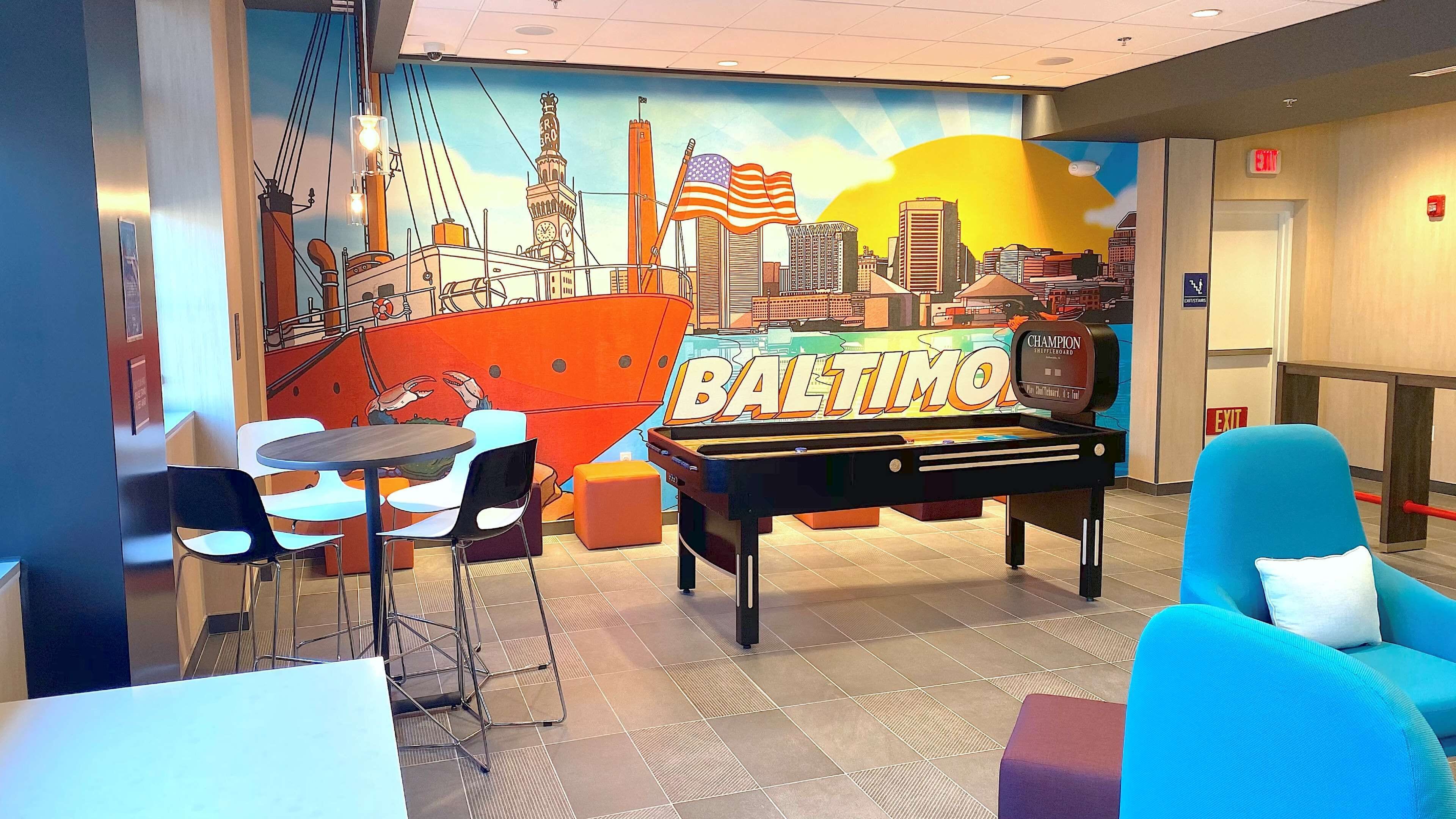 A pool table with "BALTIMORE" on it, surrounded by chairs and a mural of a cityscape with a ship.