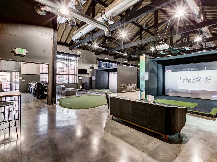 A spacious indoor area with a reception desk, seating, and a large screen displaying 'FULL SWING SIMULATORS'.