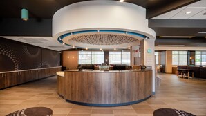 A modern hotel reception area with a central desk, seating area, and large windows. - Tru By Hilton Baltimore Harbor East, MD (Baltimore)