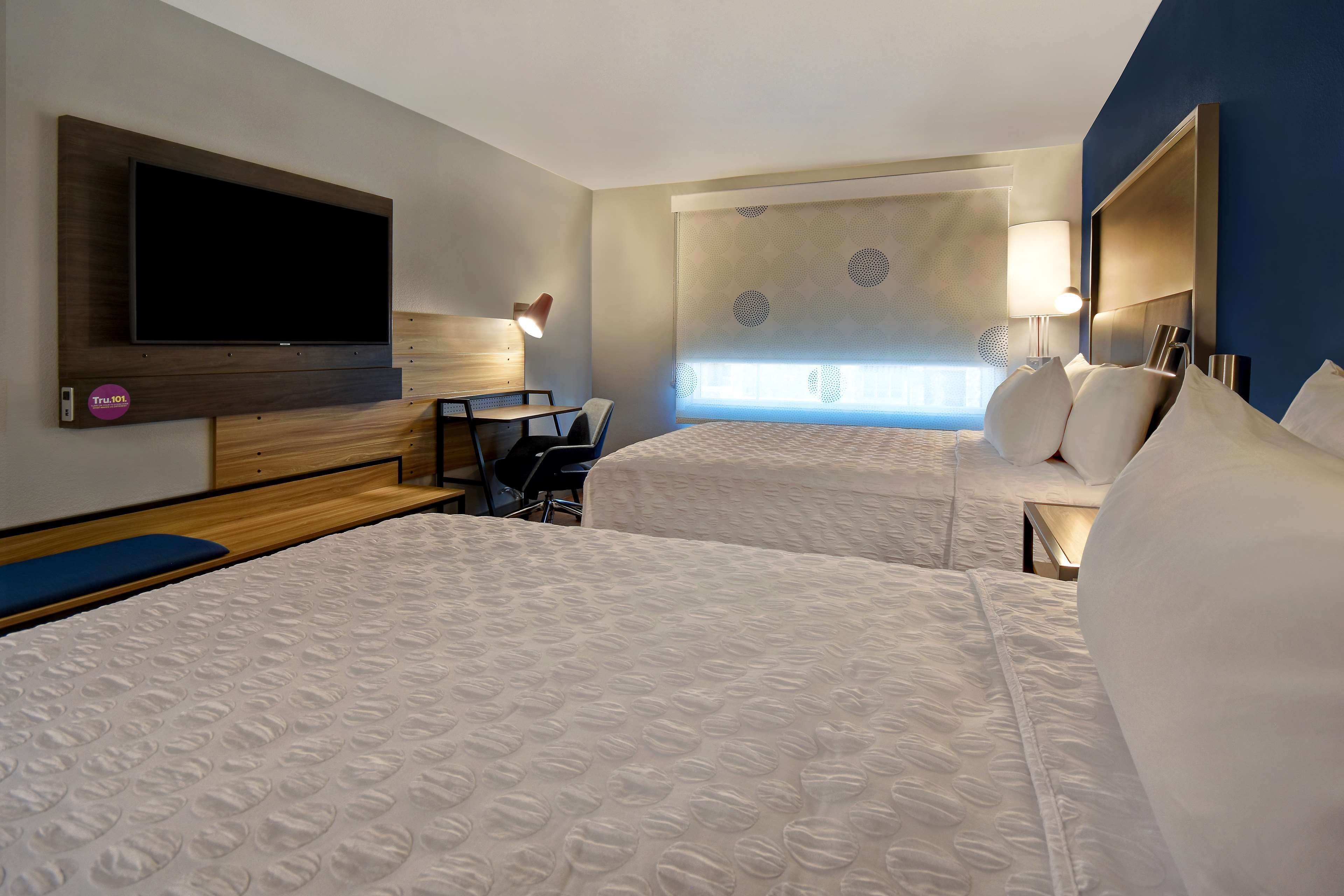 A hotel room with two beds, a TV, a desk, and a chair.