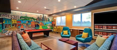 Un espace lounge animé, doté d’une table de billard, de canapés colorés et d’une fresque représentant un paysage urbain.
