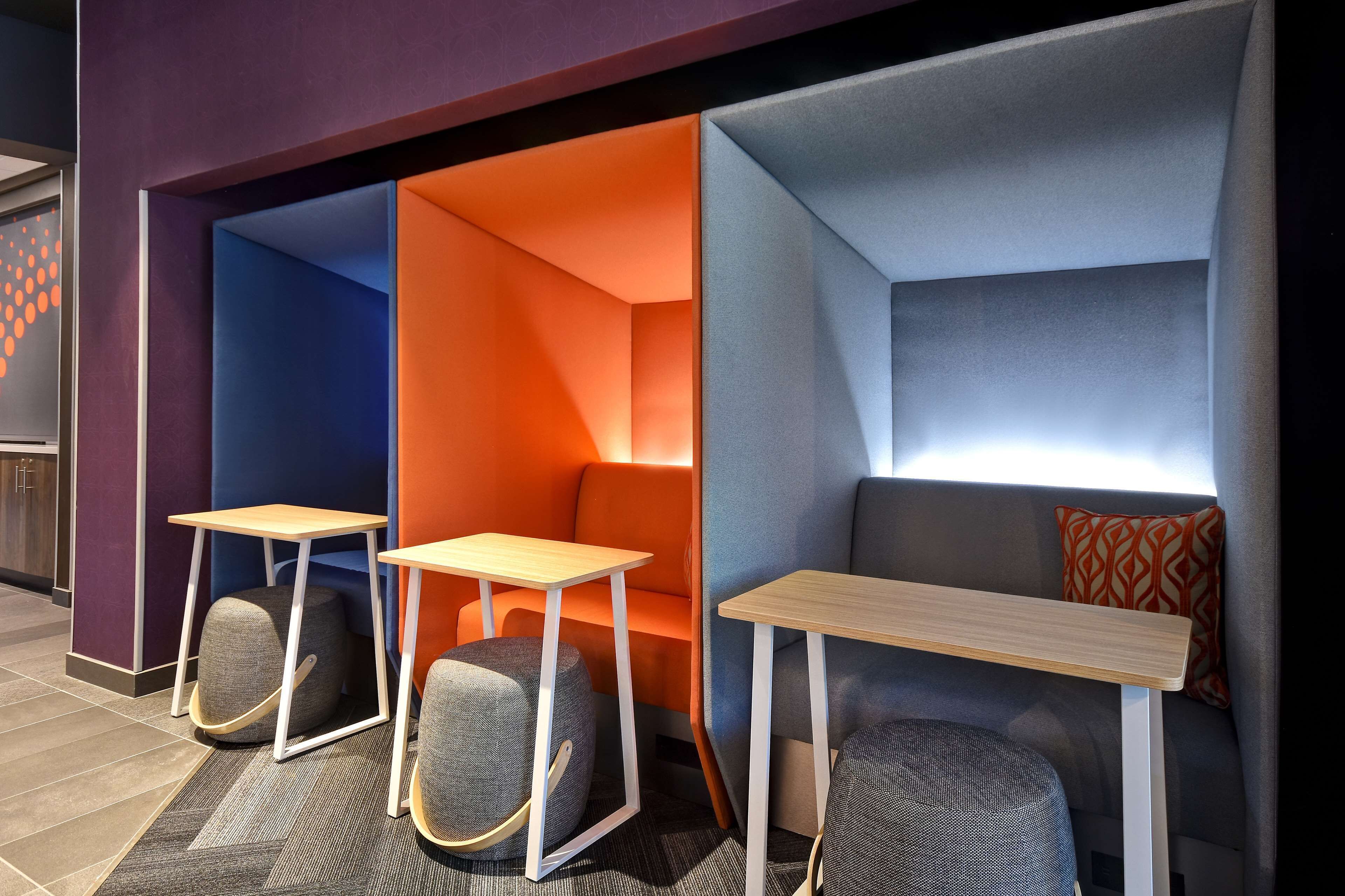 A modern seating area with cushioned chairs and tables, featuring geometric wall designs and a mix of warm and cool tones.