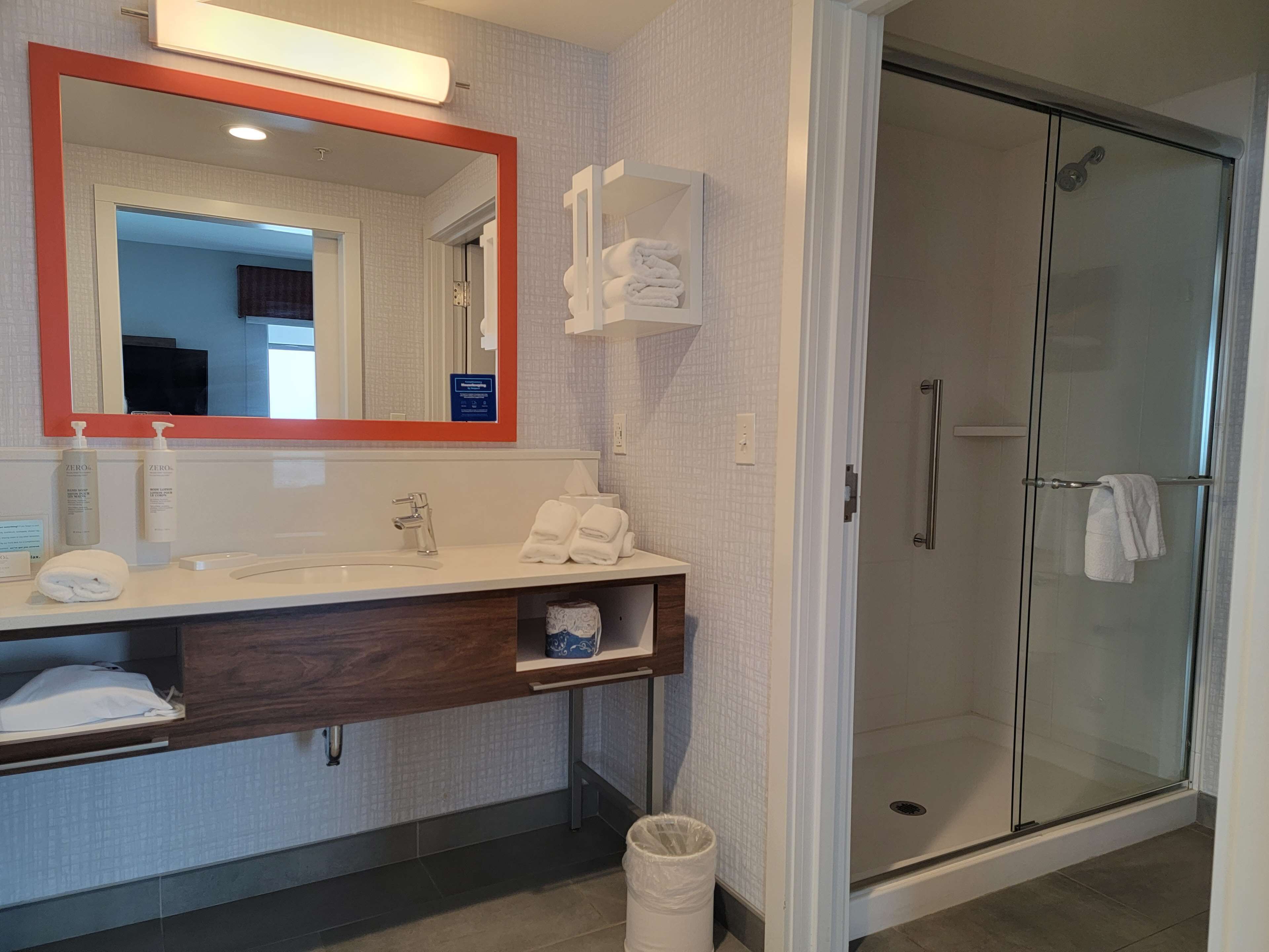 A modern bathroom with a large mirror, a shower, and a vanity with toiletries.