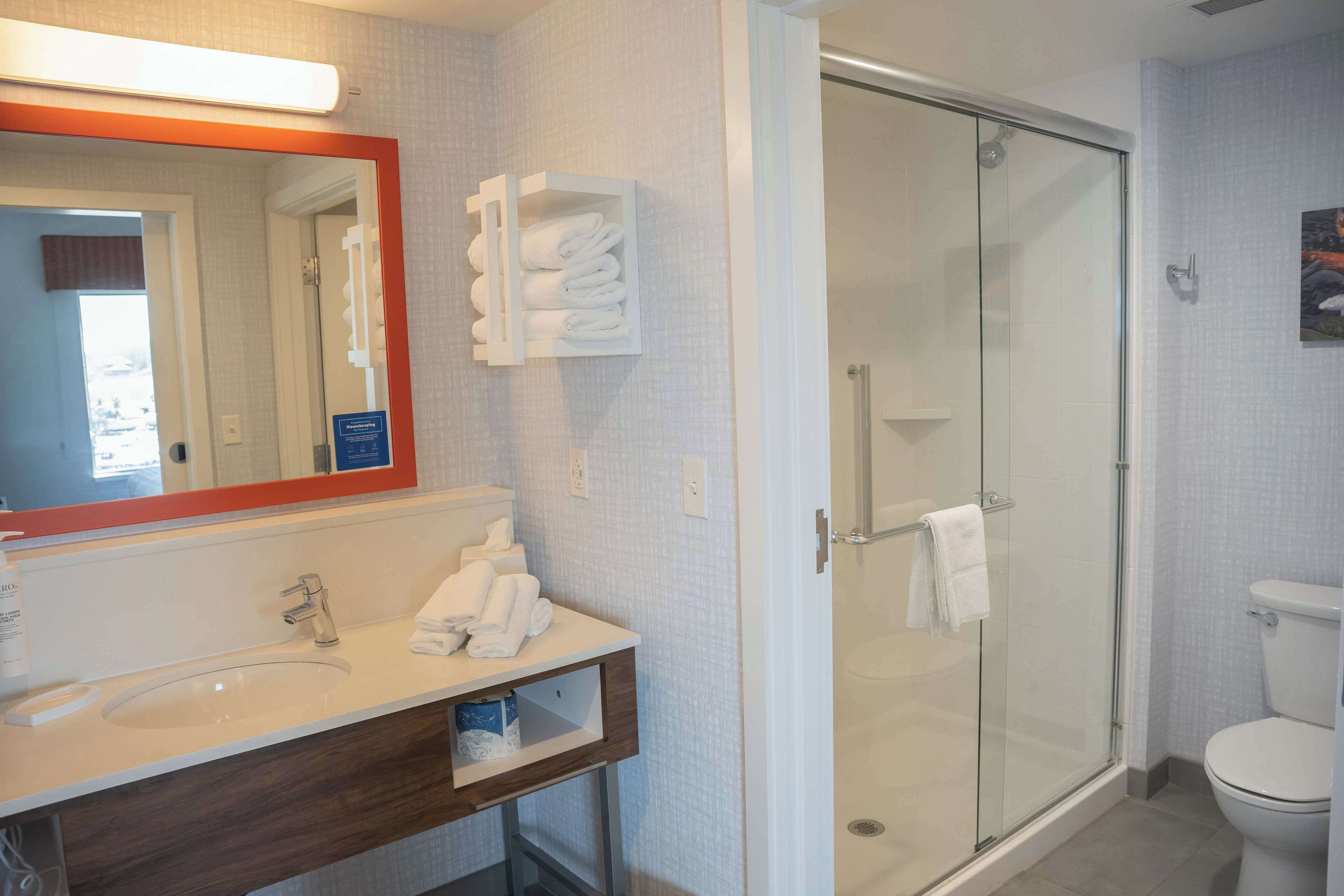 Un baño moderno con ducha de vidrio, un lavabo blanco con espejo y toallas dobladas con cuidado.