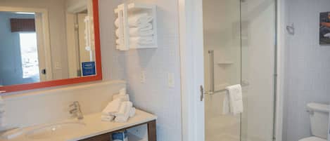 Un baño moderno con ducha de vidrio, un lavabo blanco con espejo y toallas dobladas con cuidado.