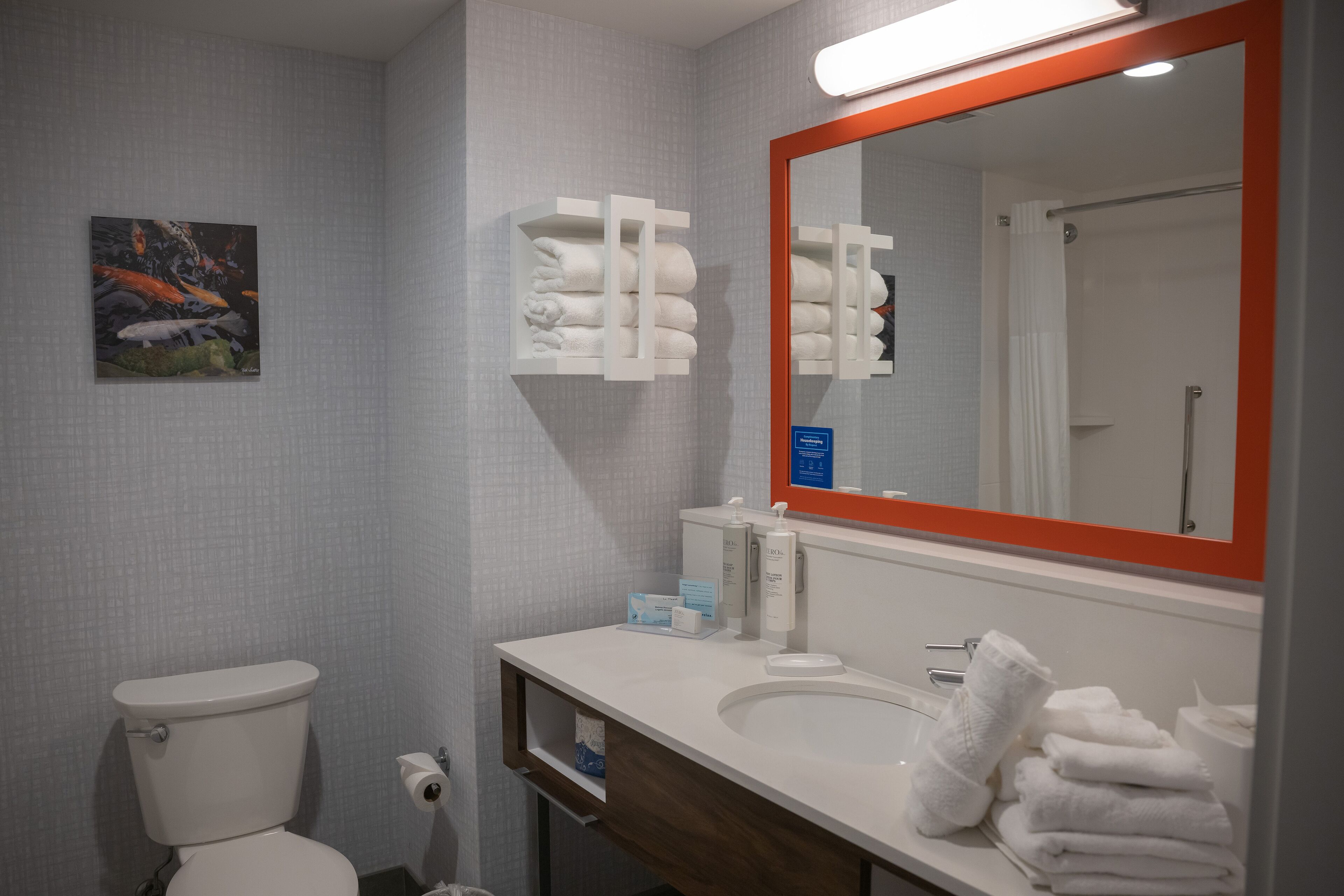 A bathroom with a toilet, sink, mirror, towel rack, and a framed artwork on the wall.