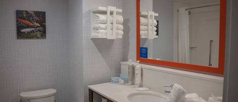 A bathroom with a toilet, sink, mirror, towel rack, and a framed artwork on the wall.