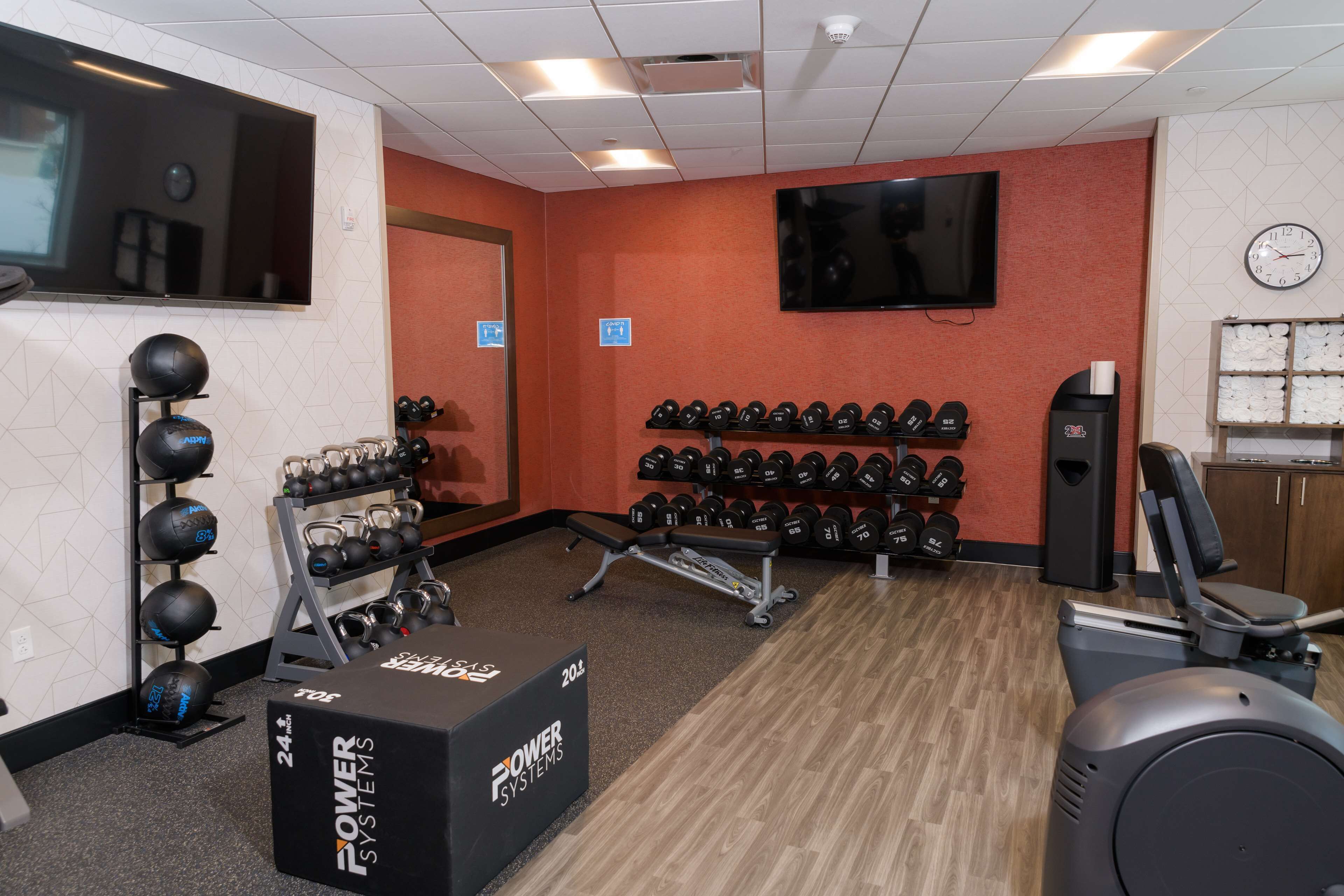 Een sportschool met trainingsapparatuur, een televisie en een klok aan de muur.