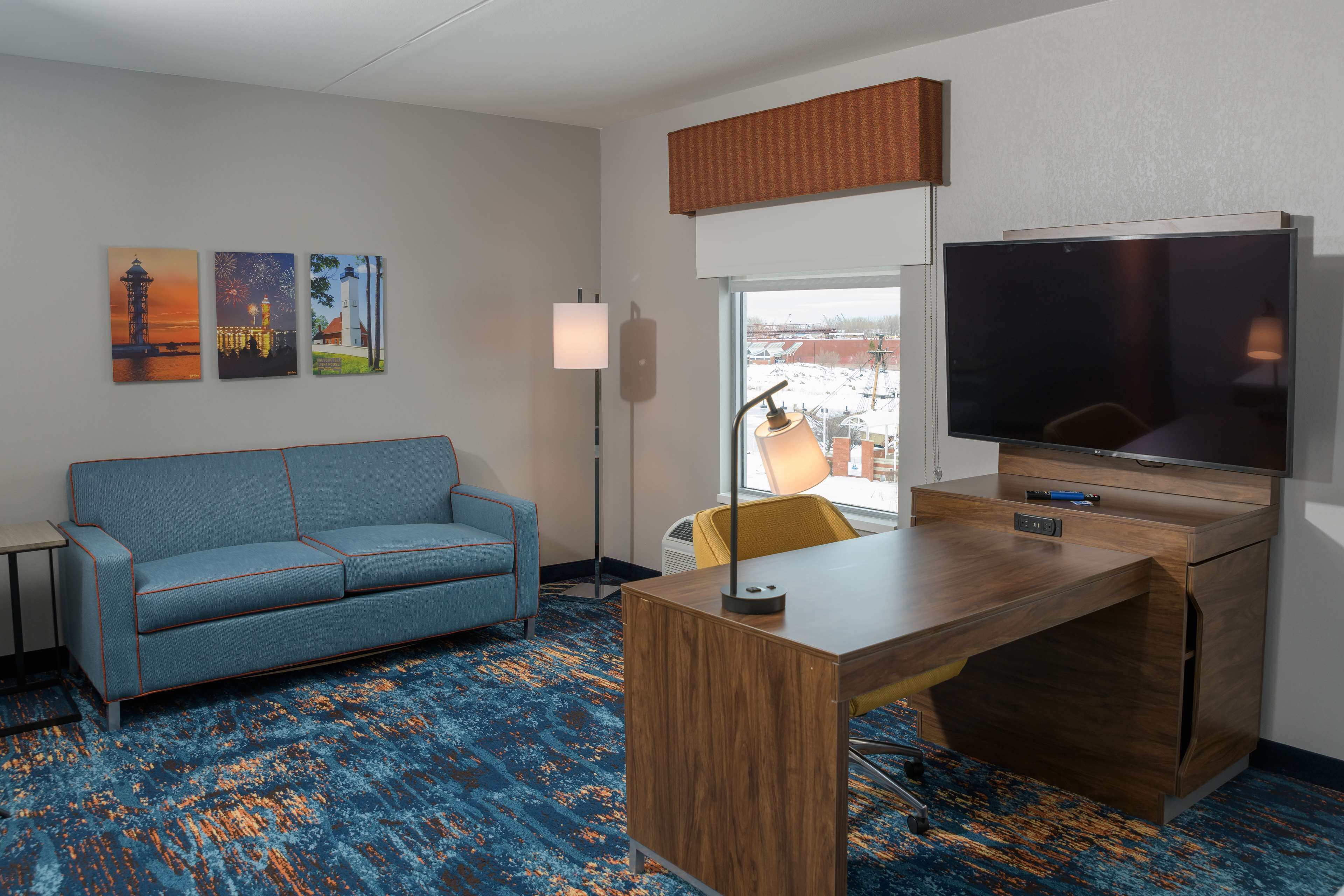 A hotel room with a sofa, a desk, a flat-screen TV, and artwork on the wall.
