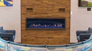A reception area with a stone wall, a fireplace, and two blue chairs. - Hampton Inn & Suites Erie Bayfront (Erie)