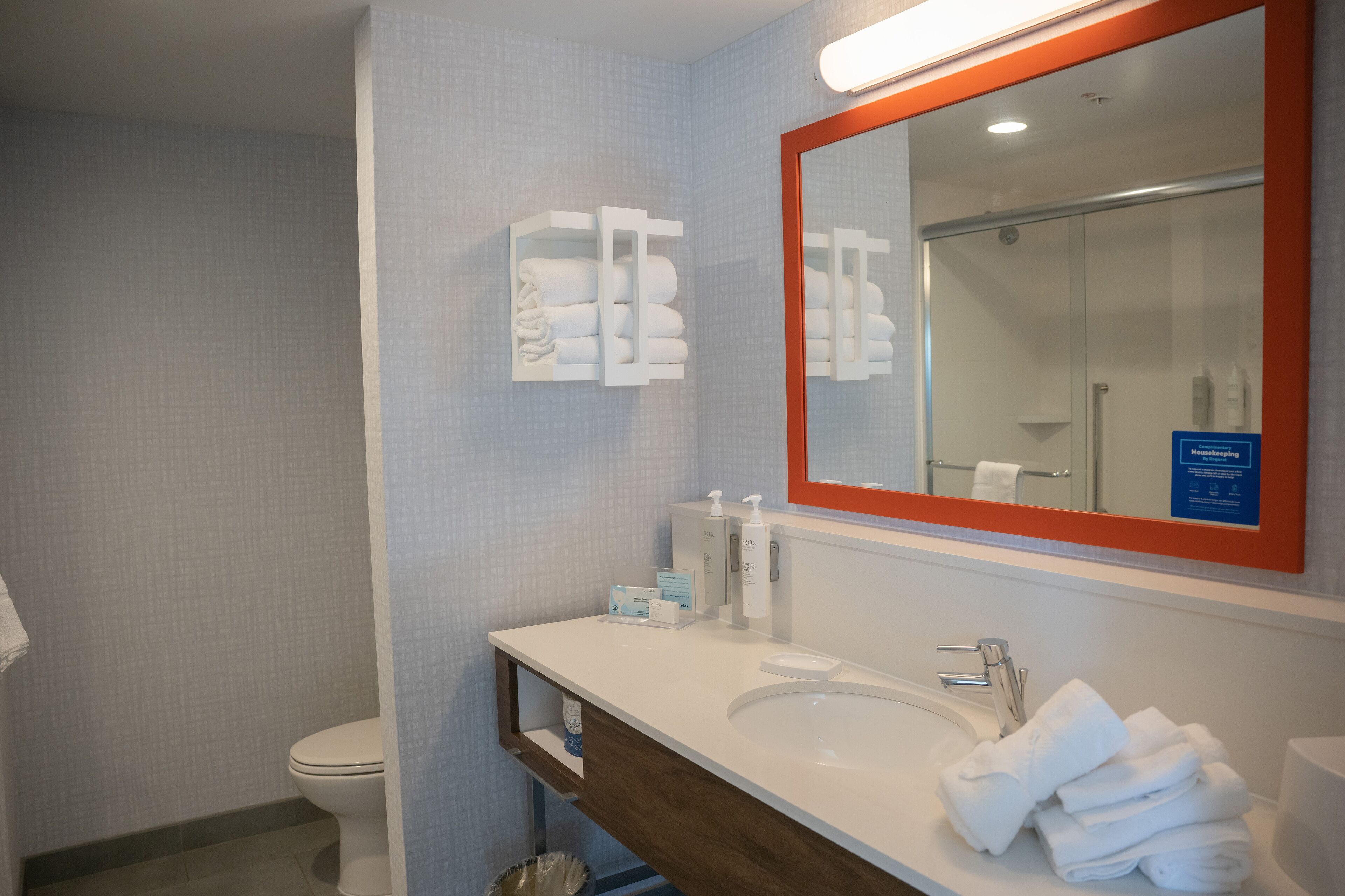 Un baño con un lavabo blanco, un espejo de marco rojo y un perchero con toallas dobladas.
