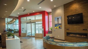 A modern reception area with a curved reception desk, a fireplace, and a large TV screen on the wall. - Hampton Inn & Suites Erie Bayfront (Erie)