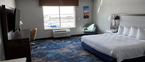 Ein Hotelzimmer mit einem großen Bett, einem Schreibtisch, einem Sessel, einem Fernseher und einem Fenster mit Blick auf die Stadt.