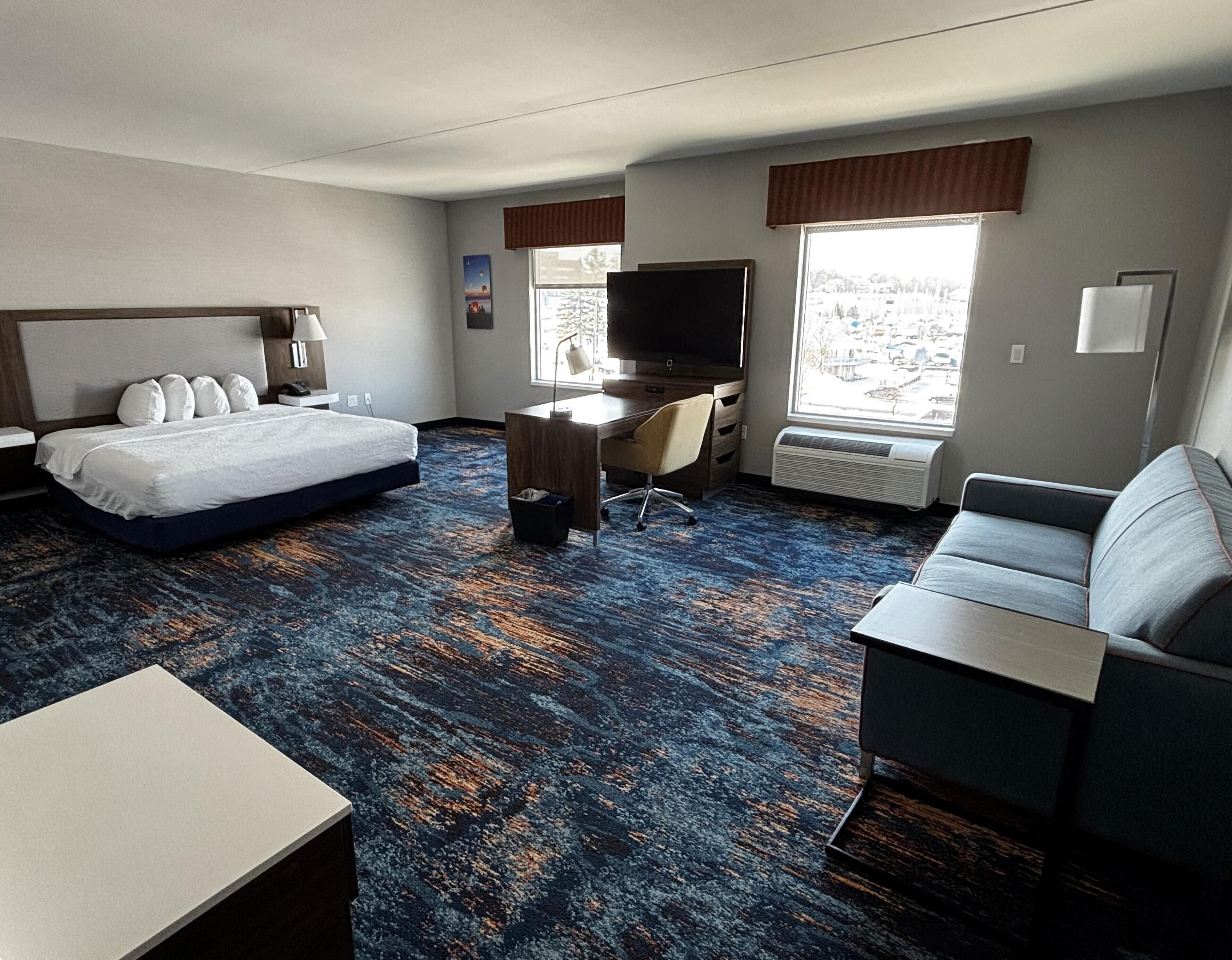 A hotel room with a bed, desk, chair, and a couch.