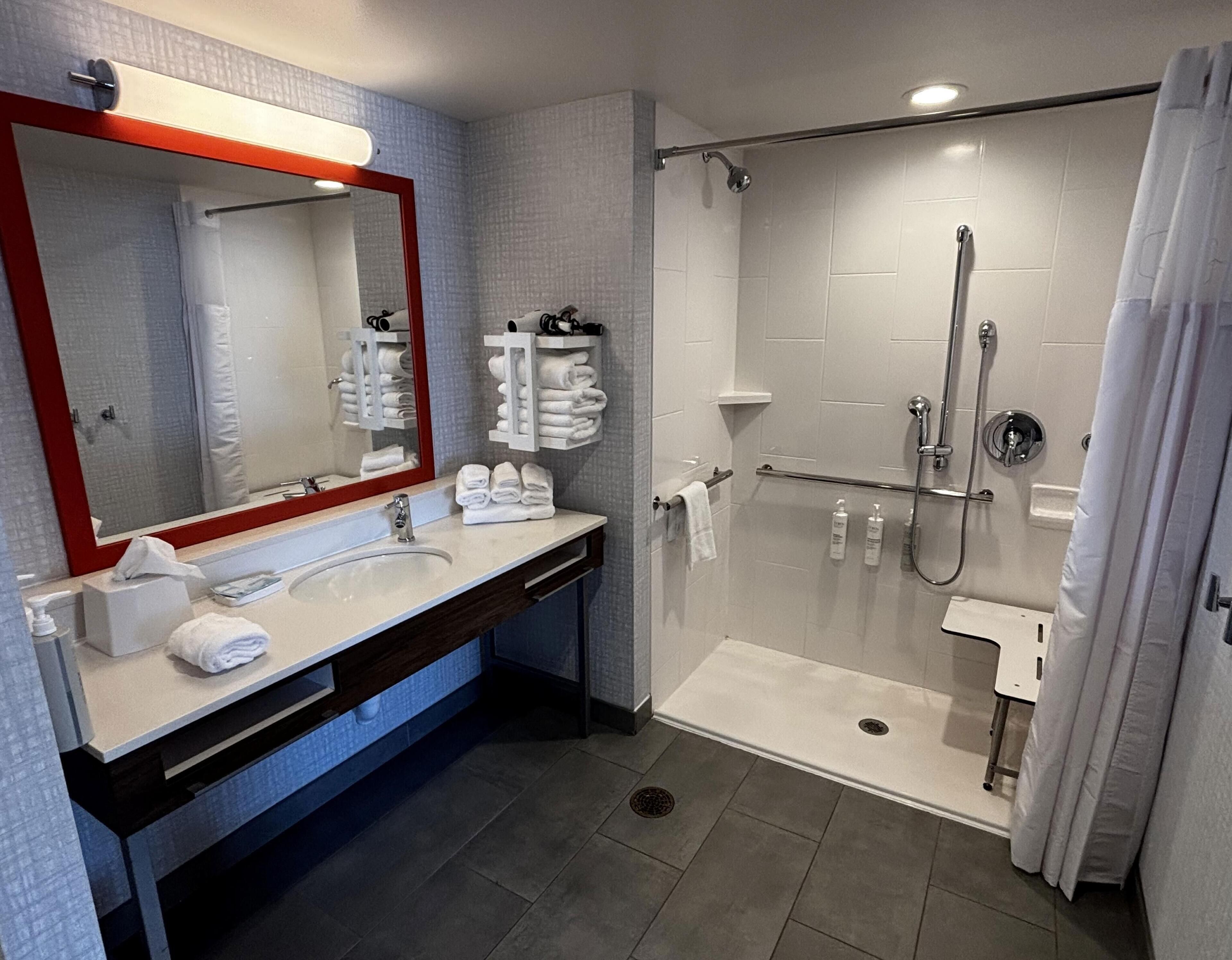 A modern bathroom with a large mirror, a sink, a shower, and a towel rack.