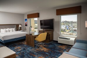 Habitación de hotel con cama, escritorio, silla, televisor y vista hacia un puerto deportivo.