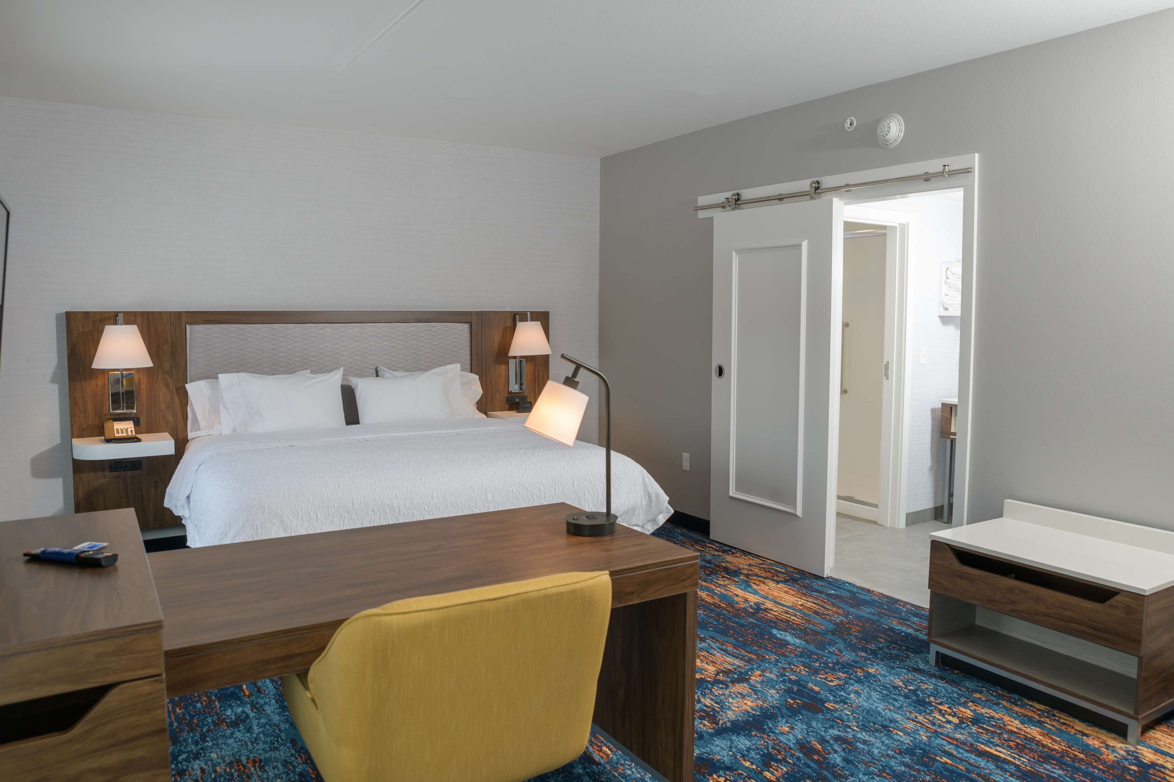 Een hotelkamer met een bed, twee bedlampen, een bureau, een stoel en een badkamer met douche en toilet.