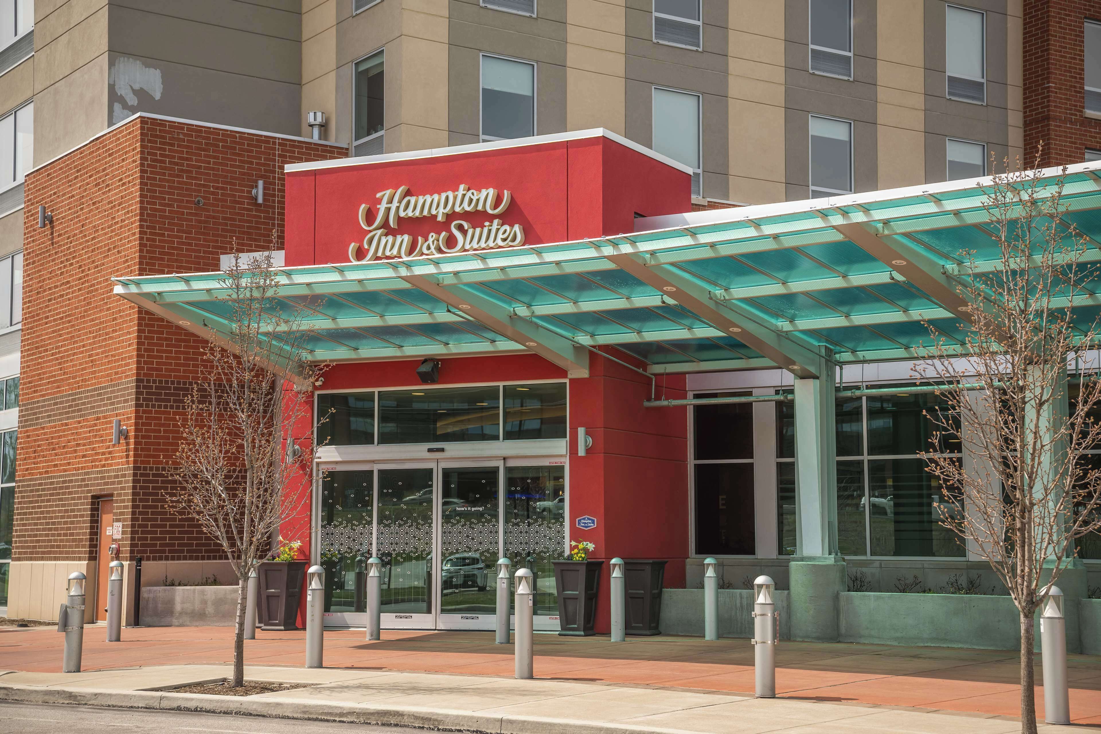 Edificio de Hampton Inn & Suites con fachada roja, grandes ventanales y un área de entrada cubierta.