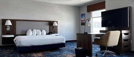 A hotel room with a bed, desk, chair, TV, and a window.