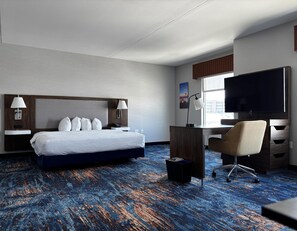Una habitación de hotel con cama, escritorio, silla, televisor y ventana.