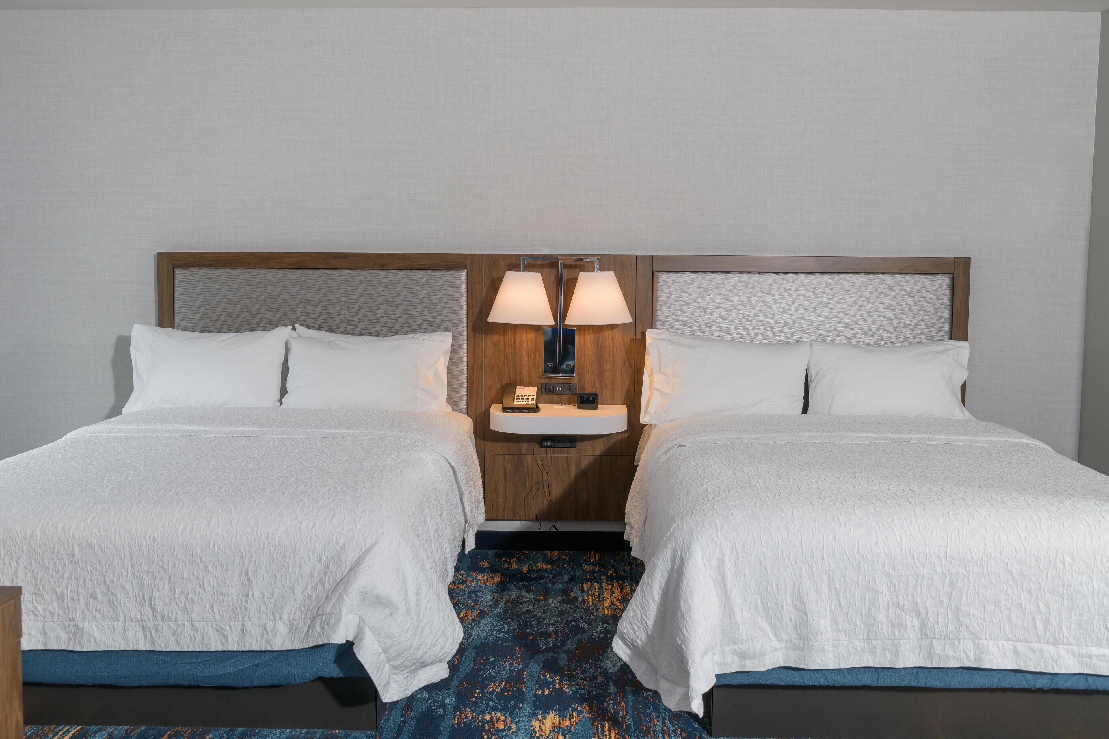 Una habitación de hotel con dos camas, una mesita de noche con lámparas y una pequeña mesa con un teléfono.