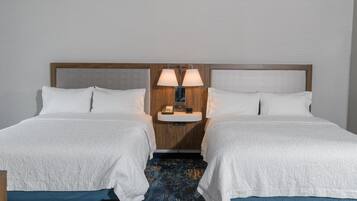 Una habitación de hotel con dos camas, una mesita de noche con lámparas y una pequeña mesa con un teléfono.