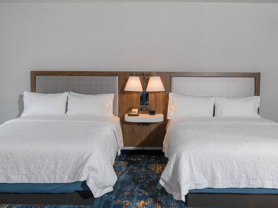 Una habitación de hotel con dos camas, una mesita de noche con lámparas y una pequeña mesa con un teléfono.
