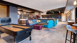 A modern lounge area with a shuffleboard table, a sectional sofa, and bar seating. - Tru by Hilton Grantville, PA (Grantville)