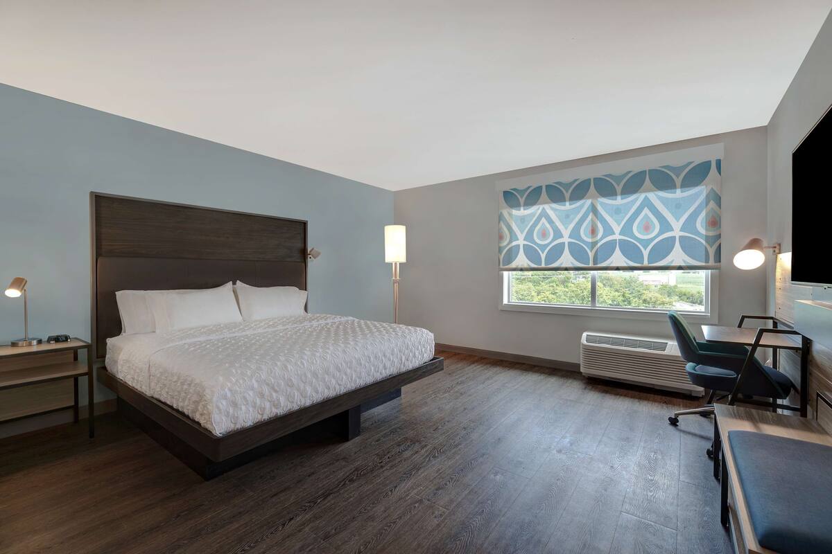 A modern hotel room with a large bed, a desk, and a chair.
