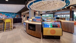 A modern interior with a central counter, seating area, and a refrigerated display. - Tru by Hilton Grantville, PA (Grantville)