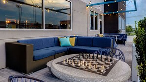 An outdoor seating area with a chess table, blue sofas, and string lights. - Tru by Hilton Grantville, PA (Grantville)