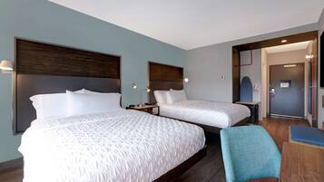 A hotel room with two beds, a blue chair, and a small table.
