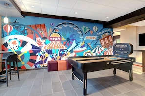 A billiards table in a room with a colorful mural featuring circus and carnival themes, including a Ferris wheel and a sign that says "PENN."