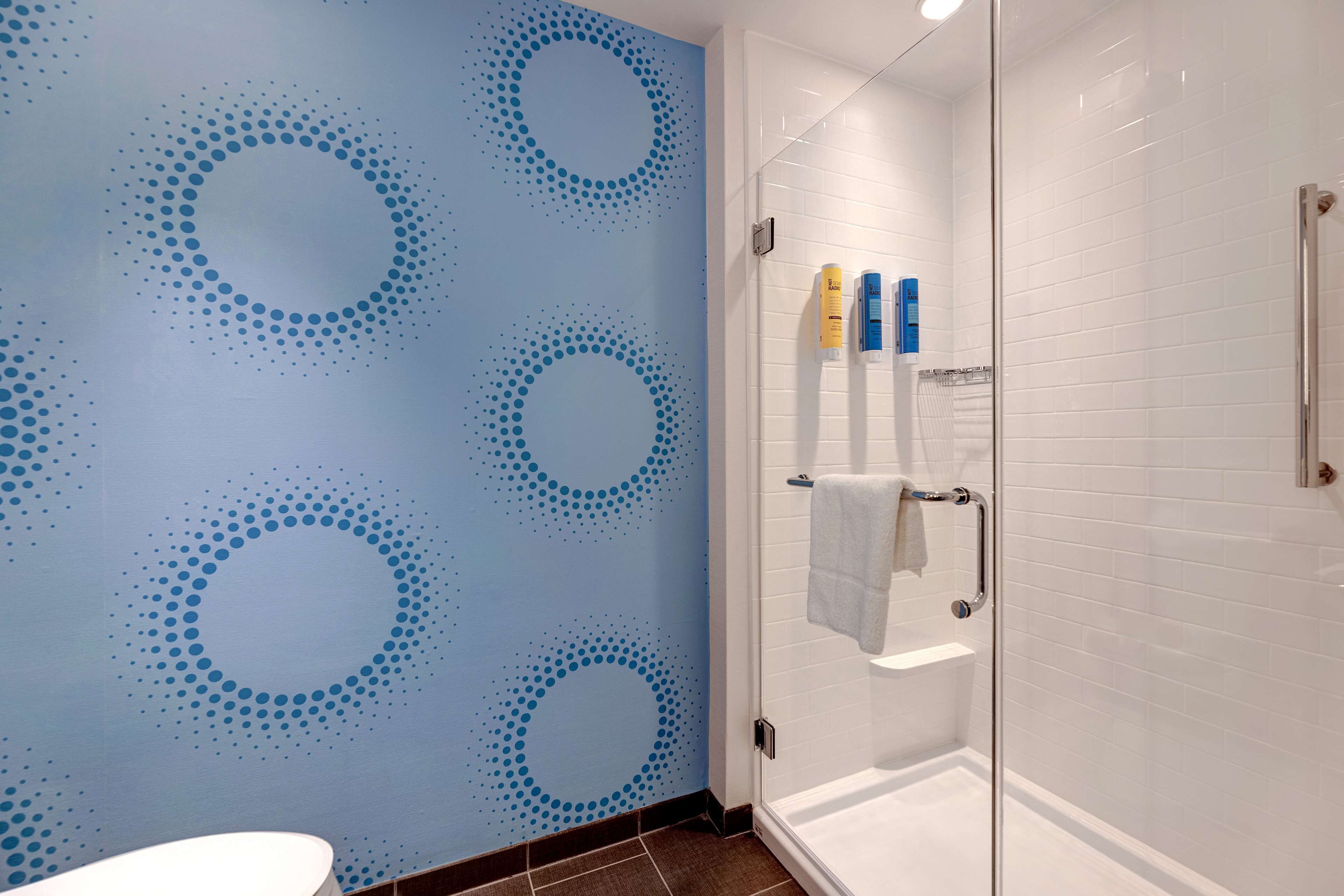 A bathroom with a blue wall featuring circular patterns, a glass shower enclosure, and toiletries on a shelf.
