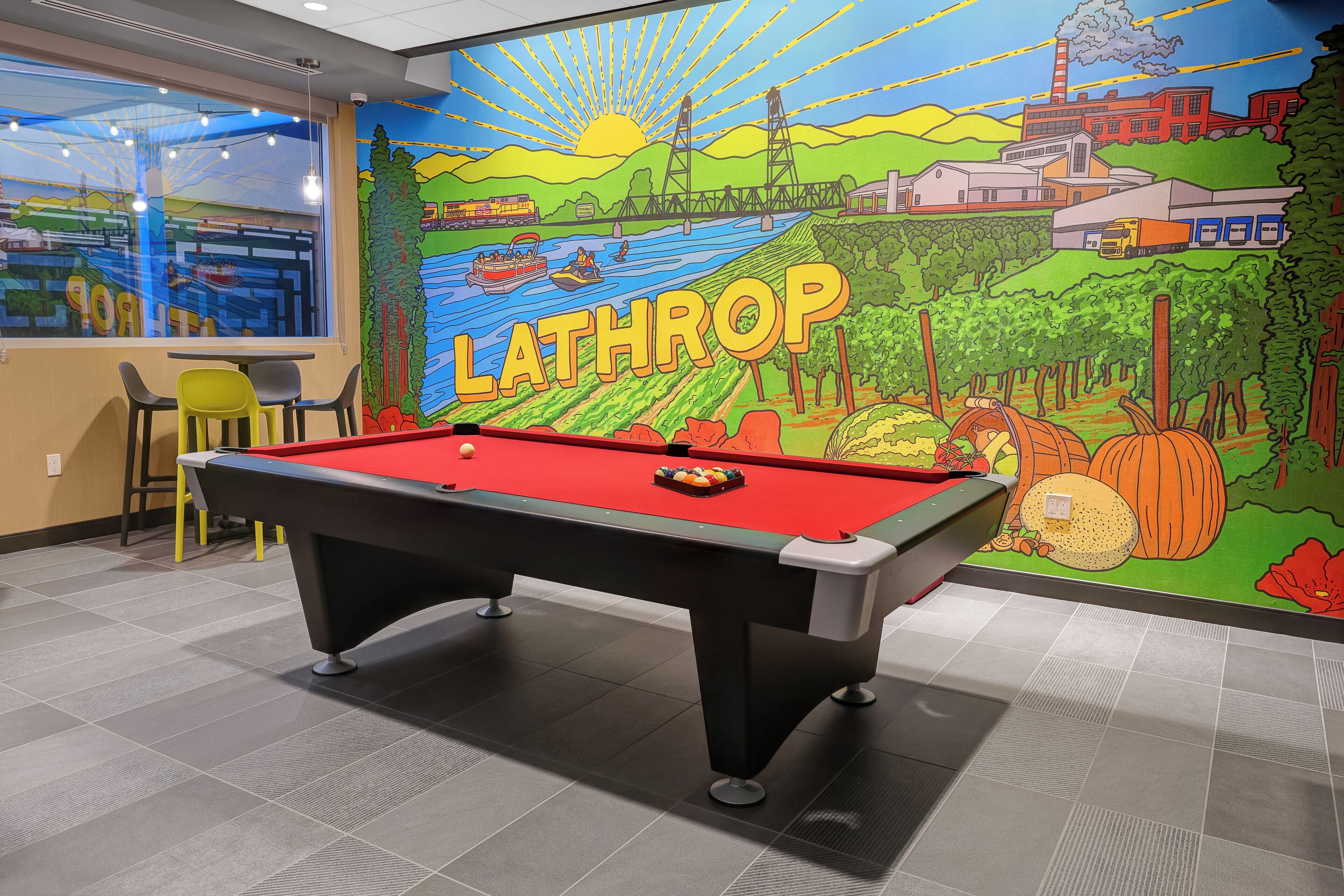 Una mesa de billar en una sala con un mural que representa un paisaje y la palabra 'LATHROP'.