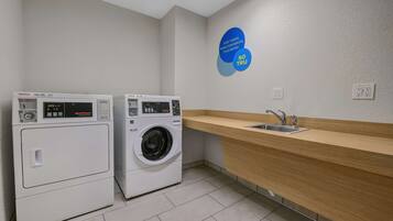 A laundry room with two washing machines, a sink, and a wooden countertop.
