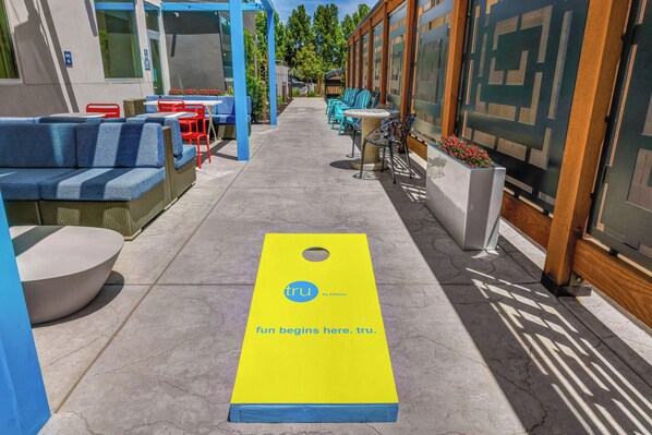 A pathway leading to outdoor seating with blue and red chairs, a yellow mat with text, and a building with patterned windows. - Tru By Hilton Lathrop, CA (Lathrop)