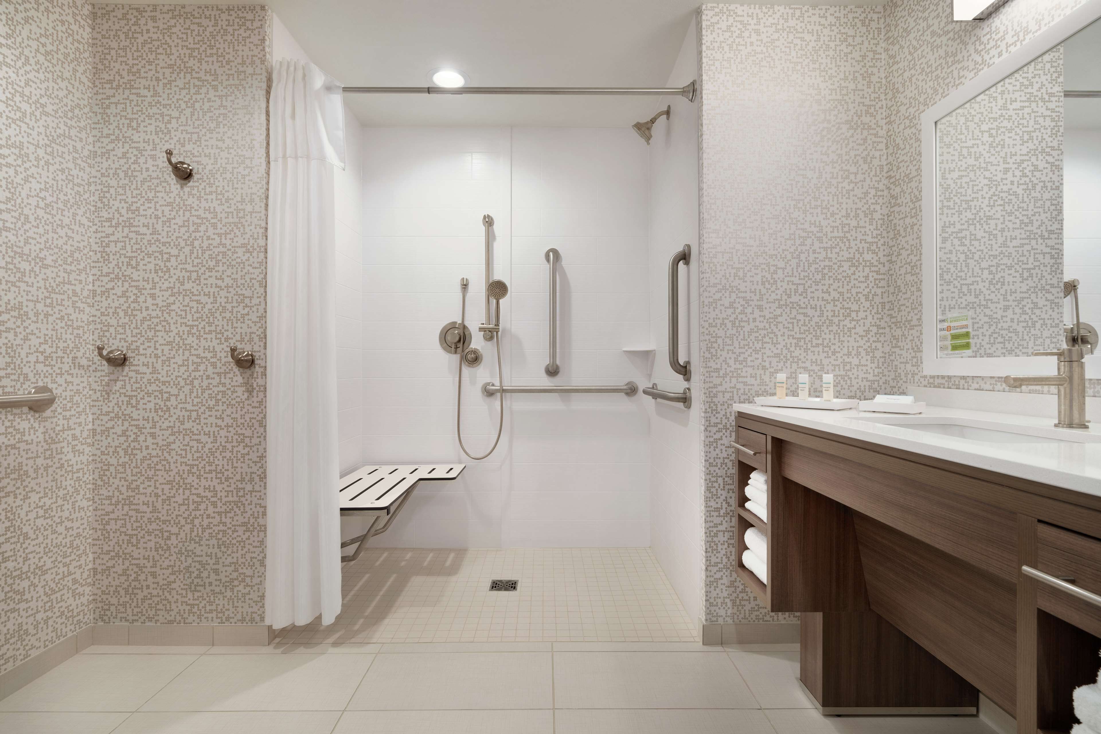 A modern bathroom with a shower, grab bars, a vanity with a mirror, and a towel rack.