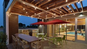 An outdoor patio with a wooden pergola, string lights, a barbecue grill, and outdoor seating. - Home2 Suites by Hilton Ephrata (Ephrata)